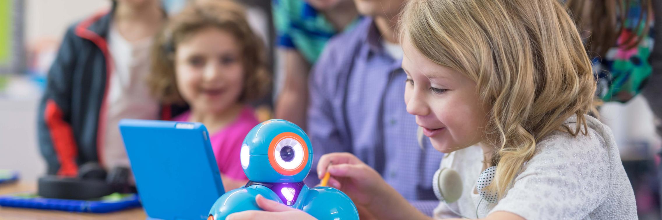 children sitting at desk with teacher fascinated by Dash robot
