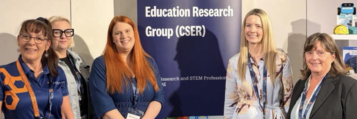 Photo of CSER staff smiling at the camera in front of CSER banner