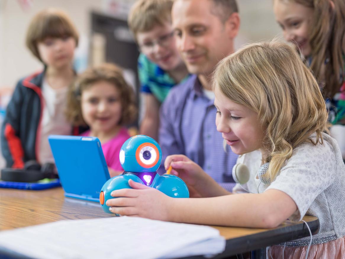 children sitting at desk with teacher fascinated by Dash robot