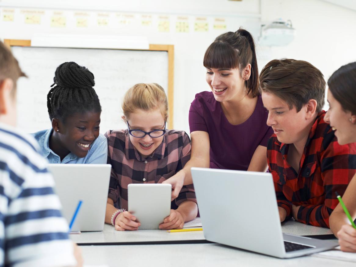 teenage students around laptops with teacher